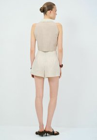 Beige mouwloos topje met een kraaghalslijn, gecombineerd met hooge taille gestreepte shorts. Draagt zwarte hakken met bontaccenten.