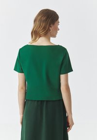 Grünes, kurzärmliges Oberteil mit einem Bootsausschnitt und einem cropped Saum. Glattes Gewebe mit leichtem Glanz, das ein einfaches Design und klare Linien aufweist.
