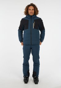 Heren geïsoleerde skijas en broek in donkerblauw met zwarte accenten, voorzien van een ritsborstzak en een hoge kraag voor extra warmte.