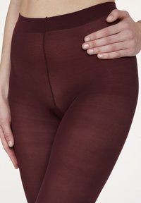 Bordeauxfarbene Leggings aus dehnbarem, glattem Material, mit einem hohen Bund und nahtlosem Design, das eng an den Beinen anliegt.