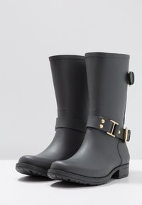 Botas de goma negras con punta redonda, altura hasta la mitad de la pantorrilla, detalle de hebilla dorada, suela texturizada y acabado liso.