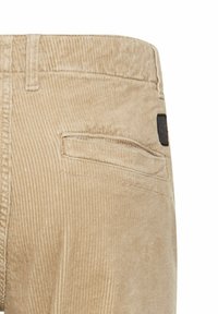Beige corduroy pants with a textured, ribbed surface. Features a back pocket and a black label on the waistband.