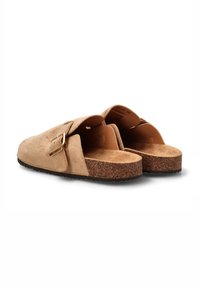Zuecos de ante beige sin cordones con un diseño redondeado, plantilla de corcho y un solo acento de hebilla metálica. Suela de goma plana con un acabado texturizado.