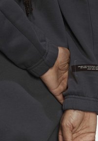 Mörkgrå sweatshirt med ribbad ärm, texturerat tyg och en etikett på sidan som visar varumärke och skötselanvisningar.