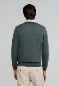 Donkergroen gebreid sweater met een ronde halslijn, lange mouwen en geribbelde boorden. Gepaard met lichtbeige broeken met zakdetails.