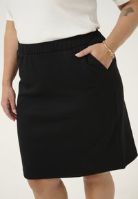 Jupe noire, longueur genou, fabriquée en tissu doux avec une taille élastique et une poche latérale. Texture lisse sans motifs ni accents visibles.
