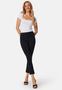 Zwarte op maat gemaakte broek met uitlopende pijpen, hoge taille en zichtbare naaddetails, gecombineerd met een aansluitend wit T-shirt met korte mouwen.