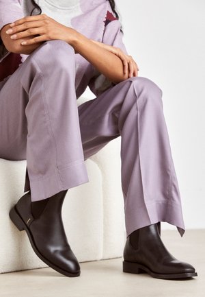 Bruna läderstövlar med slank design, rund tå och låg klack, kombinerade med lavendelfärgade vida byxor.