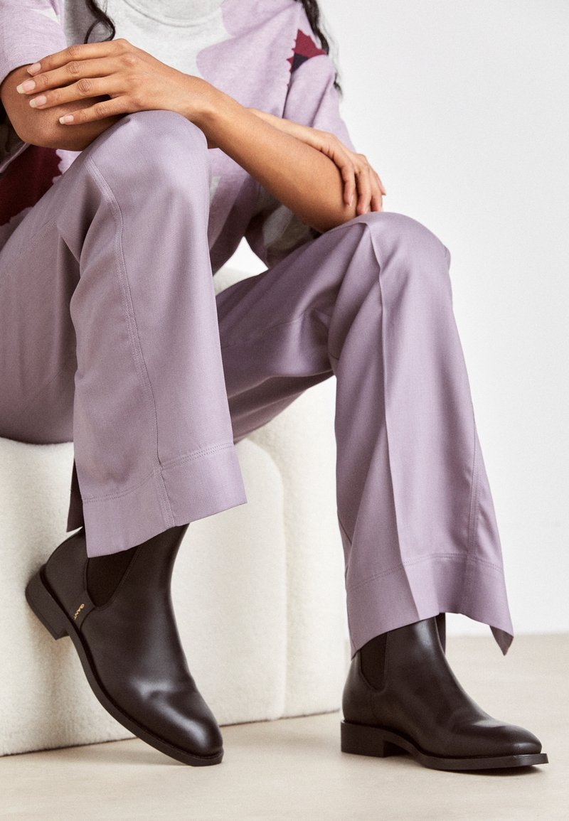 Braune Leder-Stiefeletten mit einem eleganten Design, abgerundetem Zehenbereich und niedrigem Blockabsatz, kombiniert mit lavendelfarbenen, weit geschnittenen Hosen.