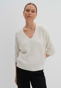 V-Ausschnitt, kurzärmeliger Pullover aus weichweißem Stoff; leicht, entspannter Schnitt mit geripptem Saum und glatter Textur.