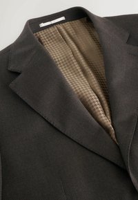 Dunkelgrauer Anzugjacke mit einem strukturierten Außenmaterial und brauner Futter im Hahnentrittmuster. Mit Reverskragen und strukturiertem Design.