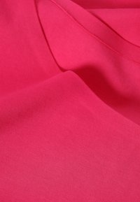 Tissu en coton rose vif avec une texture lisse, présentant des plis doux et une finition uniforme. Pas de motifs ou accents visibles.