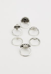 Set med sex ringar i silverfärgad metall, med olika designer, texturer och ytor, inklusive släta och mönstrade ytor.