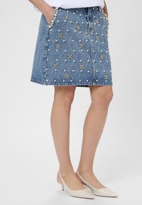 Denim mini skirt with decorative pearl and rhinestone accents; features a diamond quilted pattern, two side pockets, and raw hem.