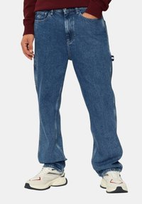 Jeans a gamba larga in denim azzurro chiaro con un classico design a cinque tasche e una leggera usura. Accoppiati con sneakers bianche e grigie.