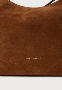 Sac à main en daim marron avec une texture lisse, présentant un design à sommet arrondi et une marque dorée "VANESSA BRUNO" à l'avant.