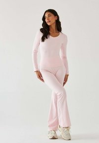 Różowa bluzka z długim rękawem i dopasowane spodnie z rozszerzanymi nogawkami wykonane z elastycznej tkaniny, zestawione z jasnymi trampkami. Prosta, gładka faktura.