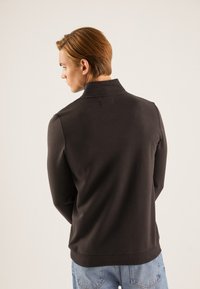Suéter negro con un cuello alto, hecho de una tela suave. Presenta un corte ajustado y un dobladillo acanalado, combinado con unos jeans azules, mostrando un look casual.