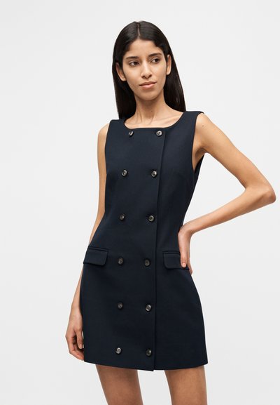 Σκούρο μπλε φόρεμα χωρίς μανίκια με ευθεία σιλουέτα, κλείσιμο με διπλό πέτο και δύο μπροστινές τσέπες με καπάκια.