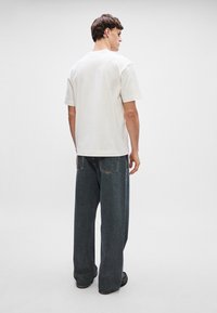 Φόρεμα σε ανοιχτό μπεζ από βαμβάκι, κοντομάνικο, συνδυασμένο με σκούρα μπλε, φαρδιά τζιν παντελόνια με ορατές ραφές και δύο πίσω τσέπες.