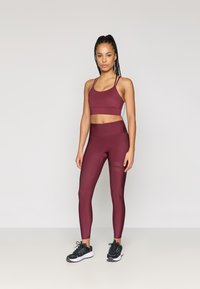 Μαρούλι αθλητικό σουτιέν και κολάν από ελαστικό ύφασμα, με εφαρμοστό σχέδιο και λεπτές τιράντες, καθώς και με υφασμάτα πάνελ. Συνδυάζεται με μαύρα αθλητικά παπούτσια.