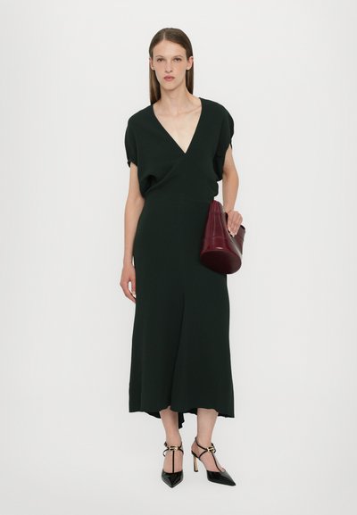 Vestido midi verde con un profundo escote en V, mangas relajadas y una silueta fluida. Combinado con un bolso burdeos y tacones negros puntiagudos.