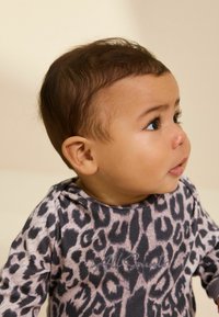 Langærmet top med leopardtrykmønster i blødt stof, der har en rund halsudskæring og ribbede manchetter. De dominerende farver er beige, grå og sort.