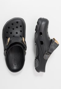 Sabots Crocs noirs avec des trous d'aération, des brides de talon réglables beige et noire, et des semelles rembourrées texturées, vus de dessus et de côté.