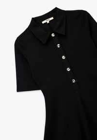 Czarna sukienka polo wykonana z gładkiego materiału, z kołnierzykiem i listwą guzikową z sześcioma metalowymi guzikami. Krótkie rękawy i dopasowany krój.