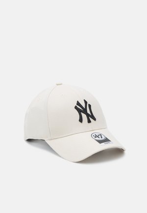 Beige baseball cap made of cotton blend, featuring black embroidered "NY" logo on front and adjustable back strap. Textured surface with ventilation holes.