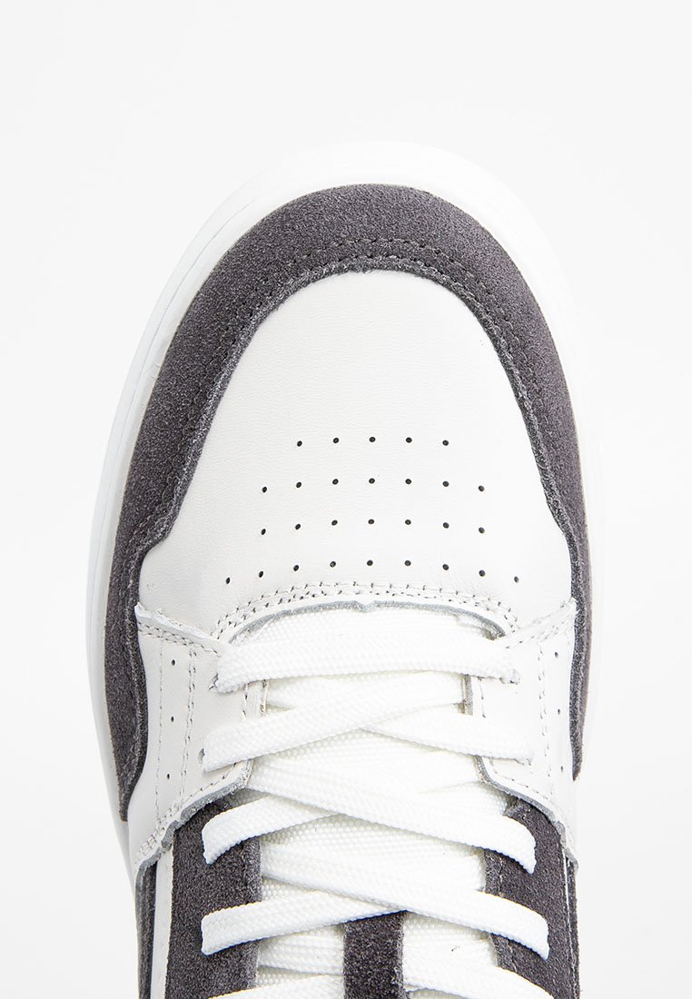 Sneaker mit einem Obermaterial aus weißem Leder und grauen Wildlederelementen, runder Zehenpartie, durchbrochenem Muster und weißen Schnürsenkeln. Texturierte Sohle sichtbar.