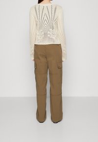 Krémový pletený svetr s otevřeným vzorem a geometrickým motivem na zádech. Olivově zelené cargo kalhoty s bočními kapsami a volnějším střihem.