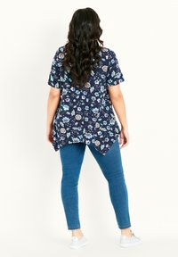 Blusa floreale blu navy con maniche corte, orlo curvo e dettaglio delle pieghe sul retro, abbinata a jeans blu attillati e sneakers bianche.