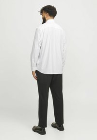 Weißes Langarmhemd mit Knopfkragen, glatte Textur, kombiniert mit schwarzen Hosen und schwarzen Schuhen. Sichtbare Nähte am Hemd.
