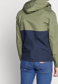 Huvjacka med tvåfärgad design i olivgrönt och marinblått, med en slät textur och justerbara detaljer.