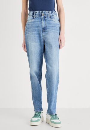 Hemelsblauwe denim jeans met een relaxte pasvorm, voorzien van een hoge taille, subtiele vervaging en twee voorkruiden. Gecombineerd met groene en witte sneakers.