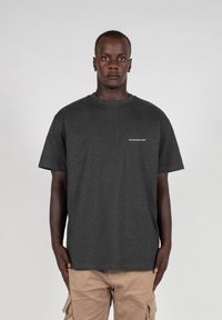Dunkelgraues Baumwoll-T-Shirt mit rundem Ausschnitt und kurzen Ärmeln, mit einem kleinen weißen Logo auf der linken Seite. Leicht und lässig geschnitten.
