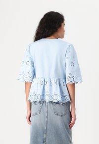 Top in cotone azzurro chiaro con maniche corte a sbuffo, caratterizzato da motivi floreali tagliati al laser all'orlo e alle maniche, design peplum.
