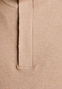 Beżowy sweter z teksturowanym wzorem i krótkim kołnierzykiem. Tkanina ma miękkie, dziane wykończenie z wzorem w kształcie diamentu.