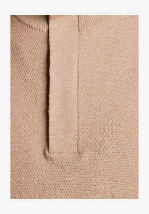 Beżowy sweter z teksturowanym wzorem i krótkim kołnierzykiem. Tkanina ma miękkie, dziane wykończenie z wzorem w kształcie diamentu.