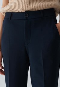 Marinblå skräddarsydda byxor i slätt tyg, med en framficka, dragkedja och en matchande knäppning.