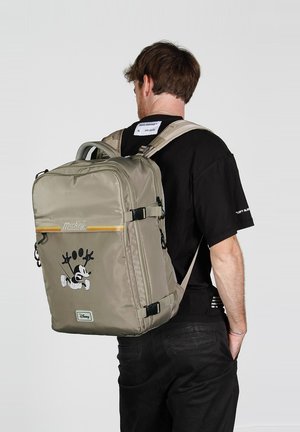 Sac à dos kaki avec une finition brillante, arborant un graphisme de Mickey Mouse, une bande d'accent jaune, des bretelles ajustables et plusieurs compartiments.