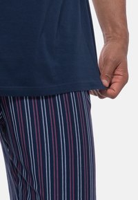 Tummansininen puuvillapaita suoremman helman kanssa, yhdistettynä tummansinisiin ja valkoisiin raidallisiin yöpaidan housuihin, joissa on punaisia yksityiskohtia. Rakenne näkyy kankaan pinnassa.