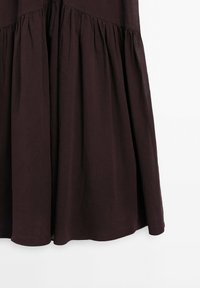 Tummanruskea mekko, jossa on kerroksellinen muotoilu, valmistettu tekstuurillisesta kankaasta. Ominaisuuksina kokoontuneet saumat ja virtaava siluetti helmassa.