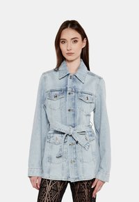 Giubbotto in denim azzurro con vita regolabile da cintura, colletto a punta e accessori in argento. Presenta due tasche sul petto e una vestibilità strutturata.