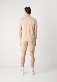 Beige bomulds T-shirt og shorts, afslappet snit, ingen synlige mustre, enkel design, parret med hvide sneakers og ankelstrømper.