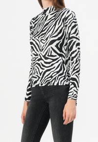 Top de manga larga y cuello alto en patrón de cebra en blanco y negro; confeccionado con una tela suave y elástica; diseño ajustado, sin cierres visibles.