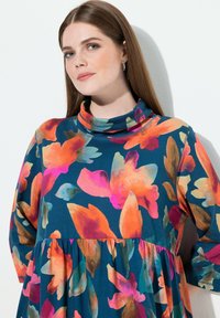 Květinové šaty s tyrkysovým základem a zářivými oranžovými a růžovými květy. Měkká látka, dlouhé rukávy a vysoký límec s nařaseným pasem.