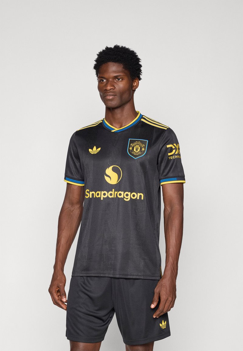 Μαύρη ποδοσφαιρική φανέλα με κοντά μανίκια, κίτρινες και μπλε λεπτομέρειες, με λογότυπο και όνομα μάρκας να προβάλλονται prominently μπροστά.