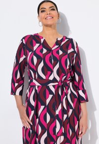 Abito stampato con un motivo astratto nei colori blu navy, rosa e borgogna, con bottoni davanti, scollatura a V e cintura in vita. Maniche lunghe con polsini.